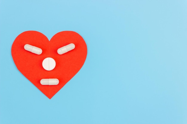 Красное сердце с лицом из таблеток на синем фоне. Концепция лекарств, пищевых добавок, витаминов для лечения сердца и профилактики заболеваний. Скопируйте пространство.