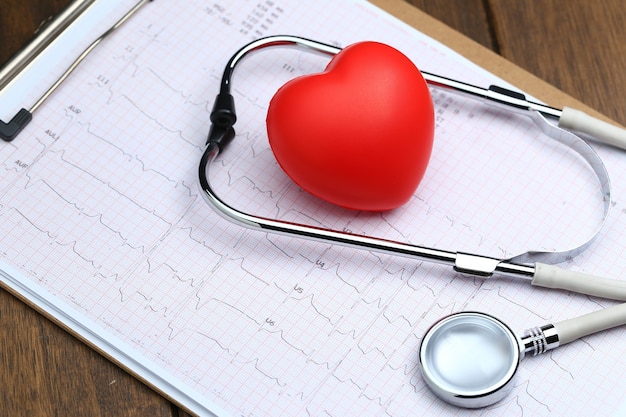 Photo red heart with stethoscope and electrocardiogram on wooden background