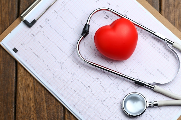 Red heart with stethoscope and electrocardiogram on wooden background