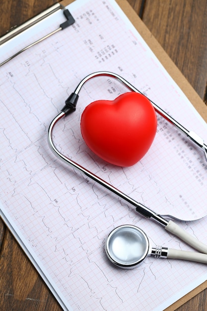 Red heart with stethoscope and electrocardiogram on wooden background