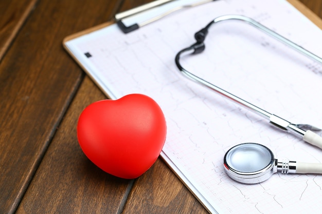 Красное сердце со стетоскопом и электрокардиограммой на деревянном фоне