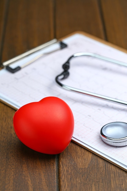 Red heart with stethoscope and electrocardiogram on wooden background