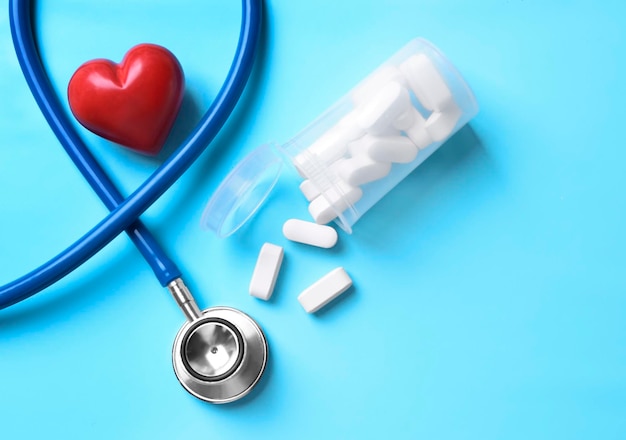 Red heart with stethoscope and pills on table