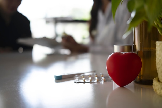 Красное сердце с термометром и медицинскими таблетками на фоне белого стола Здравоохранение и медицинская концепция