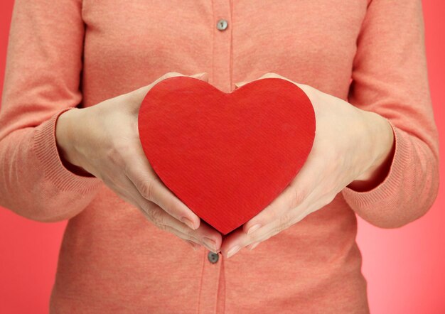 Red heart in woman hands, on red background