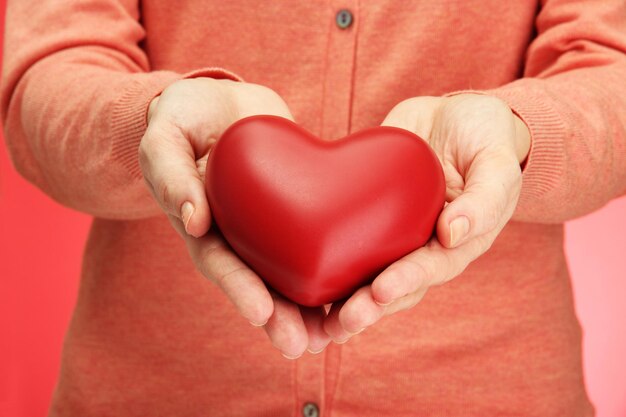 Red heart in woman hands, on red background