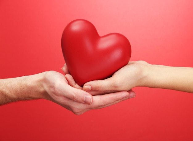 Red heart in woman and man hands, on red background