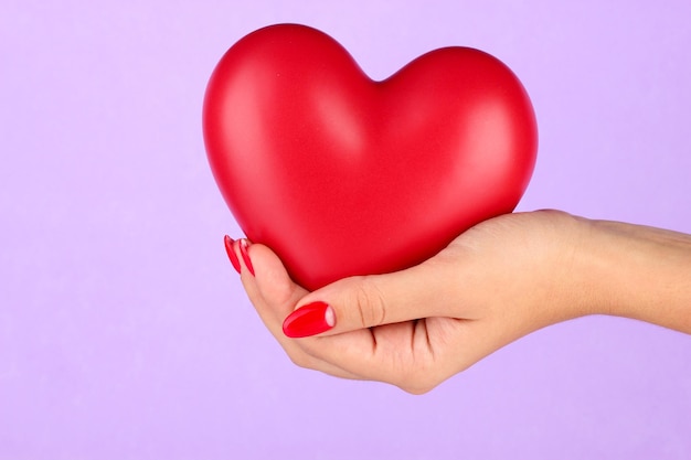 Red heart in woman's hand on color background