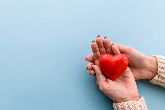 Red heart in women's hands on a blue background