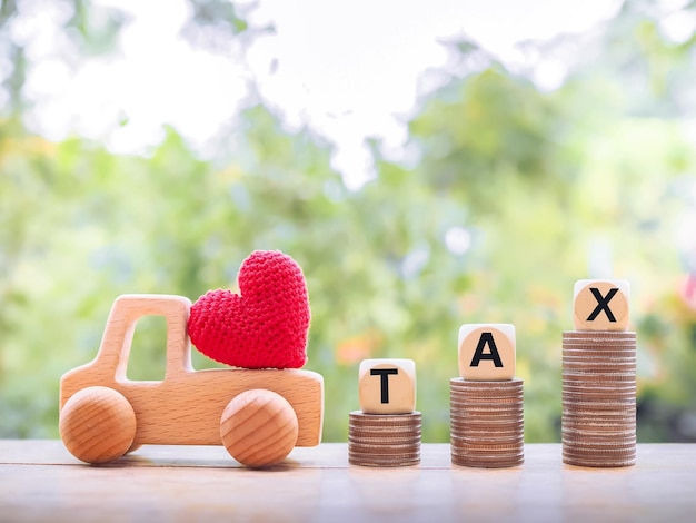 Red heart on wooden toy car, Wooden blocks with the word TAX on stack of coins