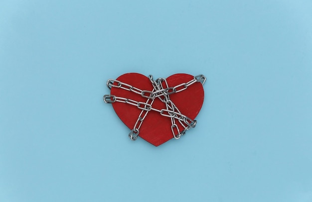 Photo red heart wrapped in a steel chain on a blue background