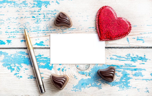 Red heartchocolate candy and pen with blank card on the old wooden background