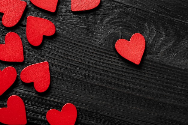 Red hearts on black wood background.