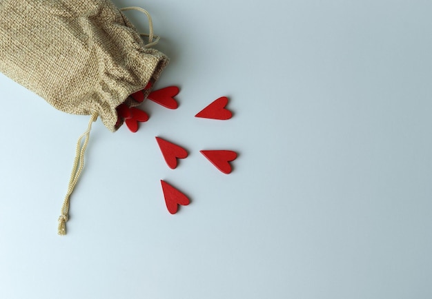 Красные сердца и тканевая сумочка с веревкой на бирюзовом фоне вид сверху Место для текста