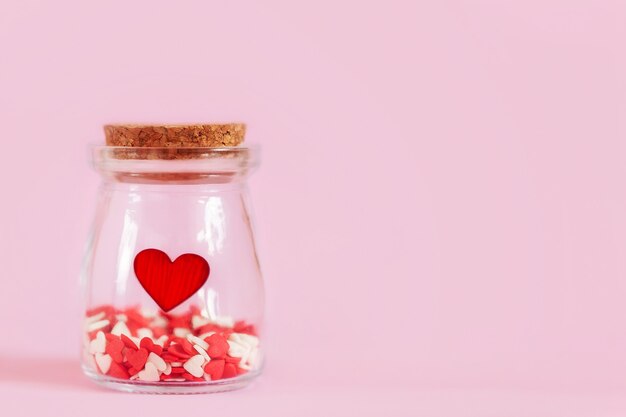 Red hearts in a glass jar on pink wall.