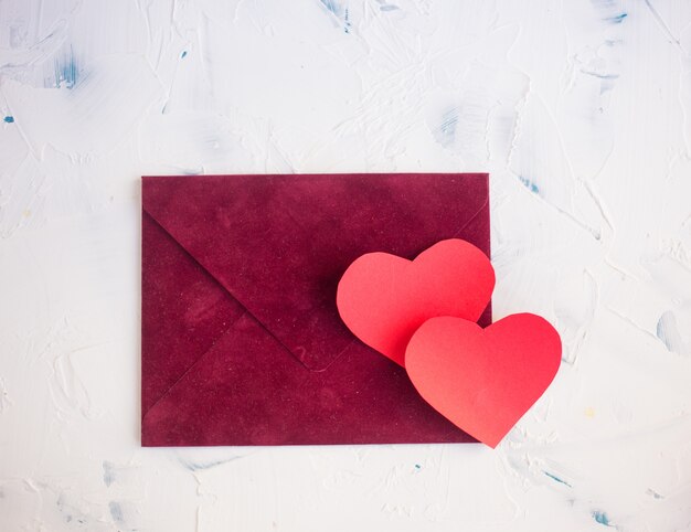 Red hearts made of paper and a gift in craft paper on a light