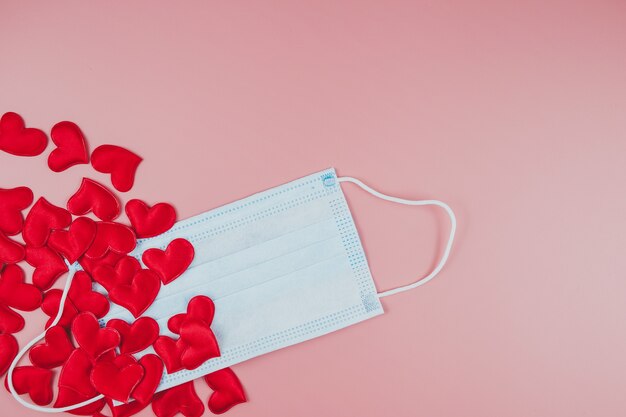 Red hearts and medical face mask on a pink background