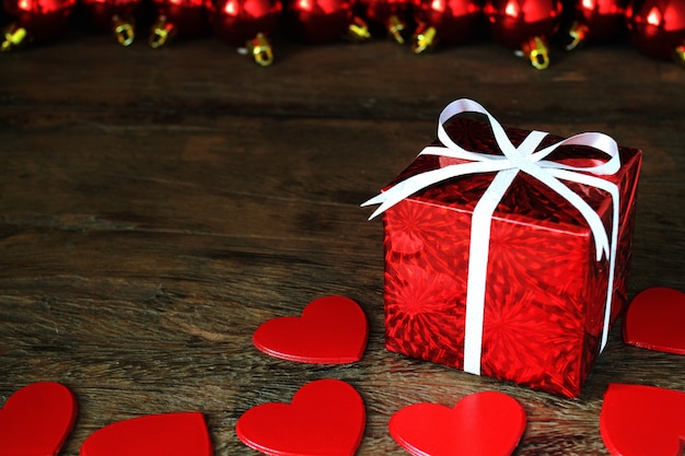 Red hearts and red gift box on wooden table.                  