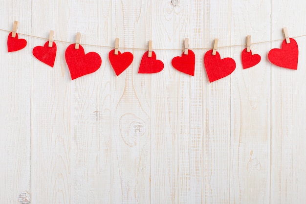 Red hearts on a rope with clothespins, on a white wooden background