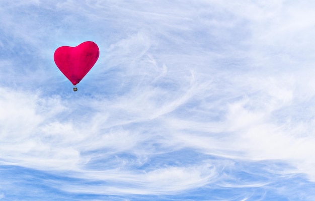 Photo red heartshaped hot air balloon flying over a blue sky with white clouds