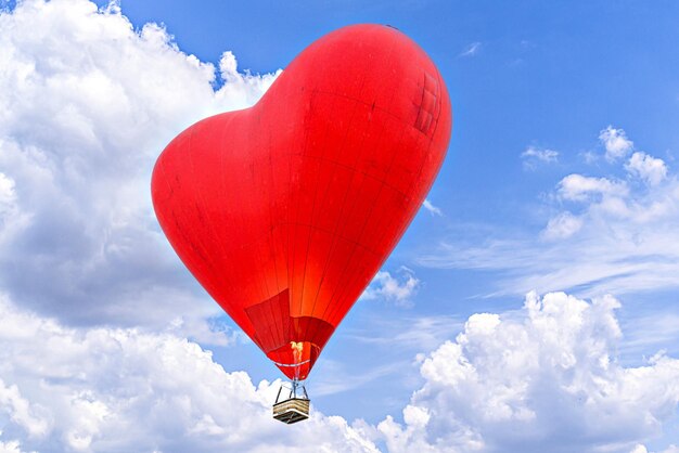 Red heartshaped hot air balloon flying over a blue sky with white clouds