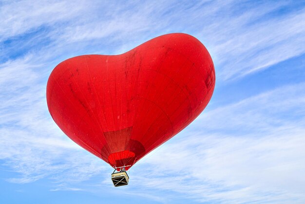 Foto palloncino ad aria calda a forma di cuore rosso che vola sopra un cielo blu con nuvole bianche