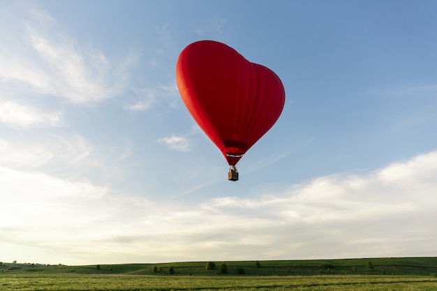 Red hot air balloon in the shape of a heart fly in sky. Love, honeymoon and romantic travel concept