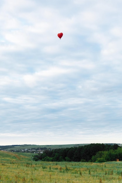 Red hot air balloon in shape of heart is landing on the green field