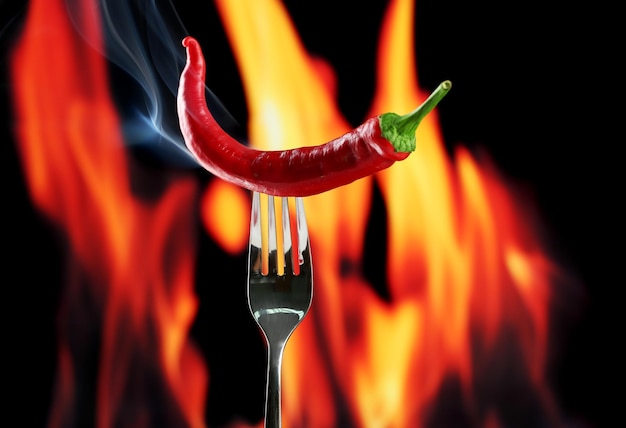 Red hot chili pepper on fork on fire background