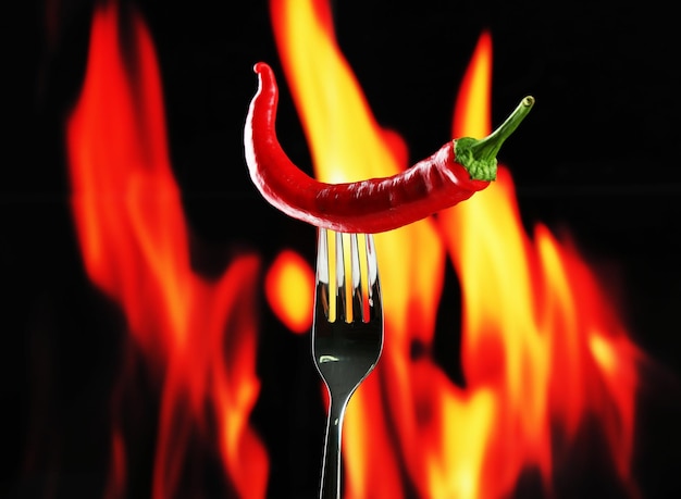 Red hot chili pepper on fork on fire background