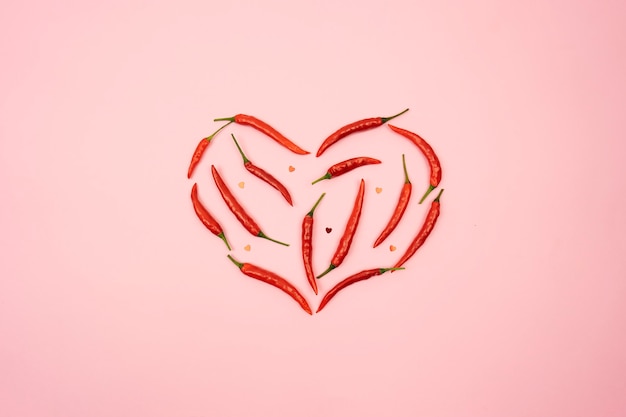 Красный острый перец чили в форме сердца лежит на розовом фоне стола