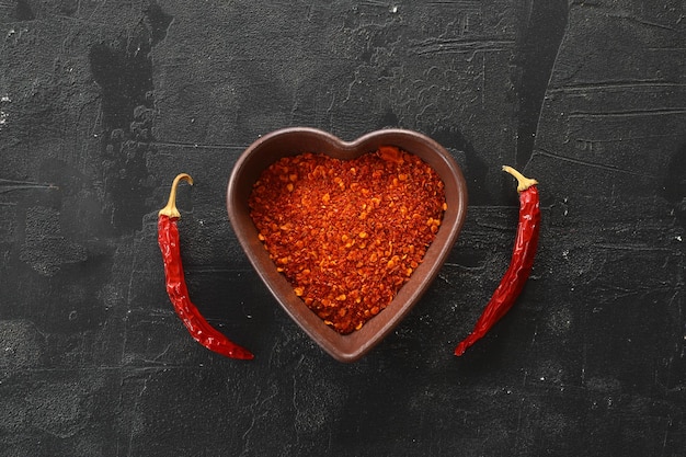 red hot chili peppers powder in heart shaped bowl on black stone table Love concept Top view