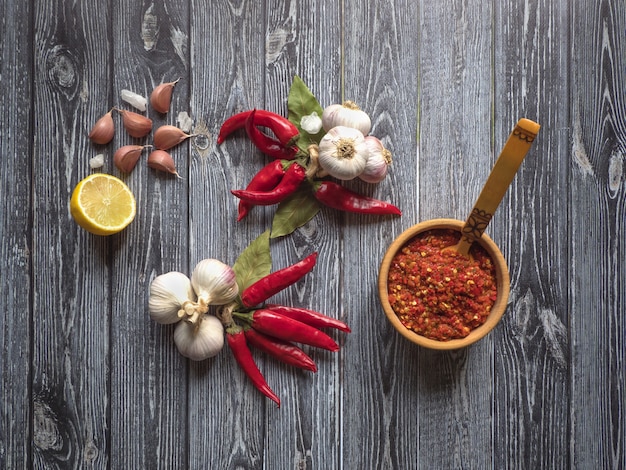 Red hot sauce, garlic, lemon, red pepper and spices on a black wooden  table. Top view.