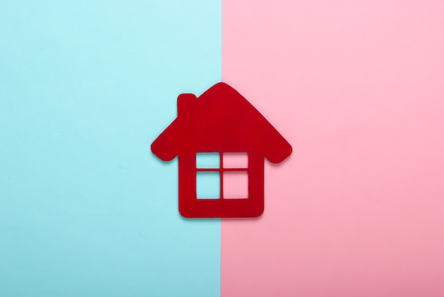 Red house figurine on pink-blue pastel background. Top view