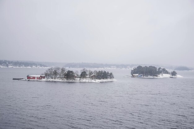 a red house is on the water with trees in the background