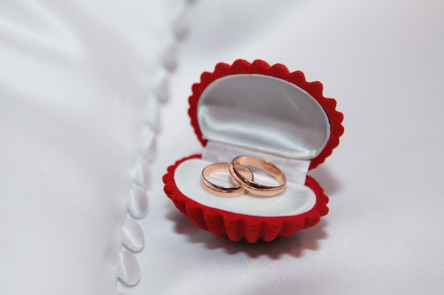 Красная шкатулка с золотыми обручальными кольцами на белой ткани