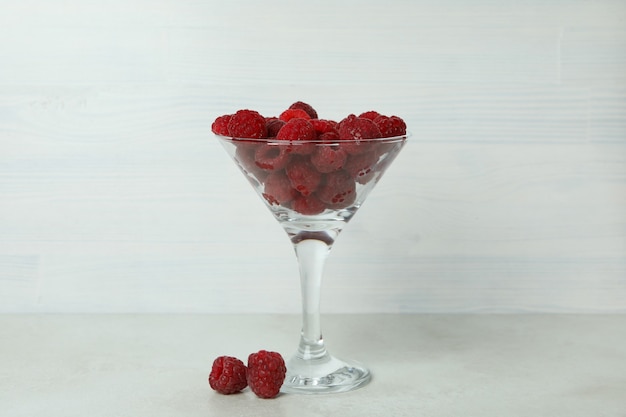 Red juicy raspberries in a glass on a white wooden background.