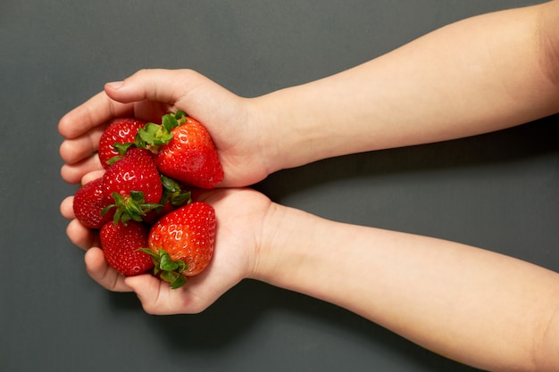 Red juicy ripe strawberries in child's hands on grey background