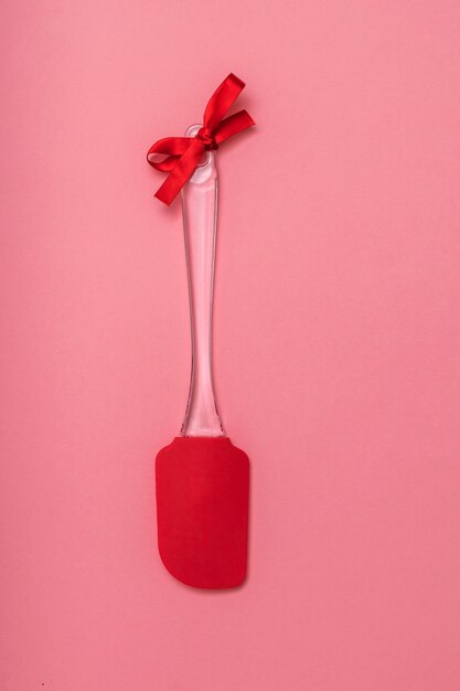 Red kitchen spatula with red ribbon on pink background. Kitchen tools on festive background. Flat lay.