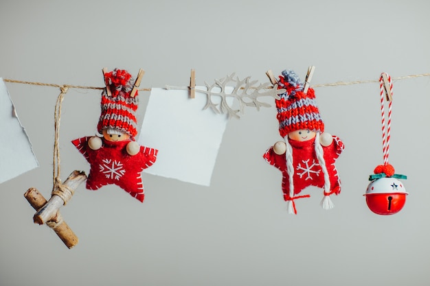 Red knitted christmas stars in funny hats. Christmas dolls and ornaments hanging on the rope with clothespin. White piece of paper for text.