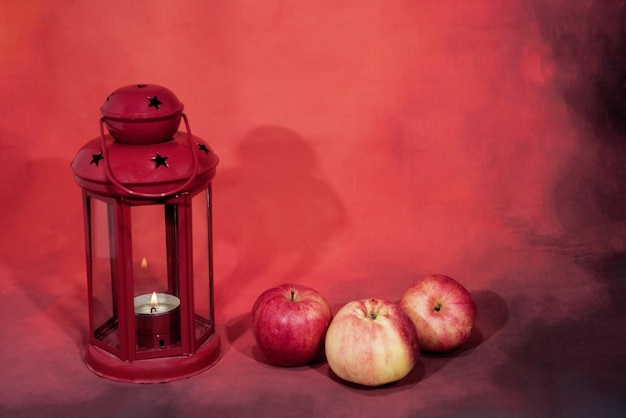 Красная лампа фонаря со свечой и яблоками.