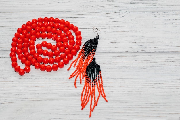 Red large beads in a necklace with handmade earrings on a wooden background.