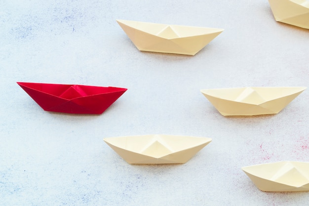 Красный лидер бумажный кораблик лидирует среди белых на текстурированном фоне