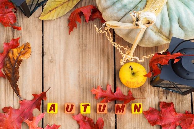 Photo red leaves, apple with lamp and colored cubes with autumn inscription