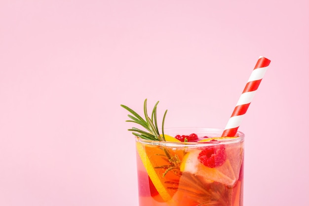 Red lemonade with lemon and raspberry decorated with rosemary\
on pink background. summer cocktail with citrus fruit and\
berries.