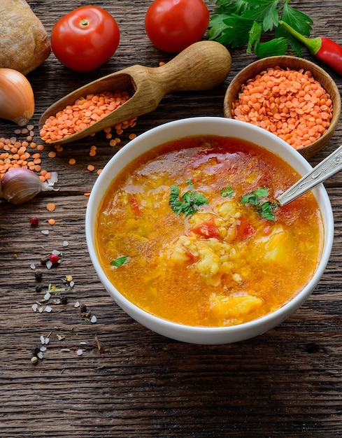 Red lentil soup in a bowl on the rustic wooden table with vegetables and spices.