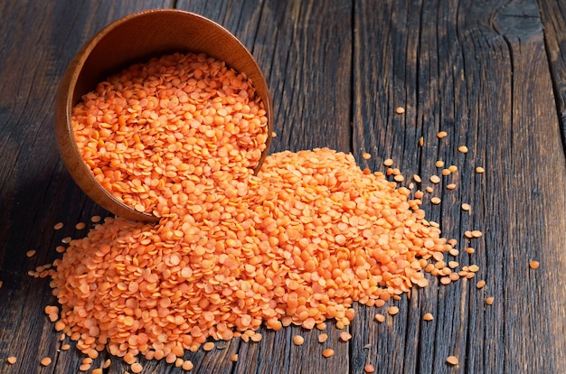 Red lentils in bowl and near on dark wooden background