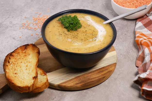 red lentils soup puree in dark bowl with bread on grey marble table