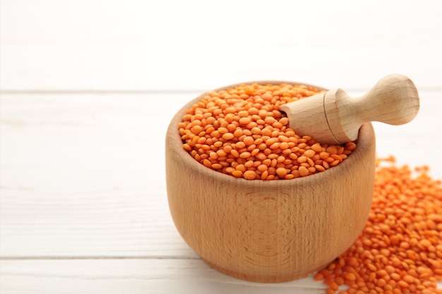 Red lentils in a wooden spoon and bowl on white wall. Close up.