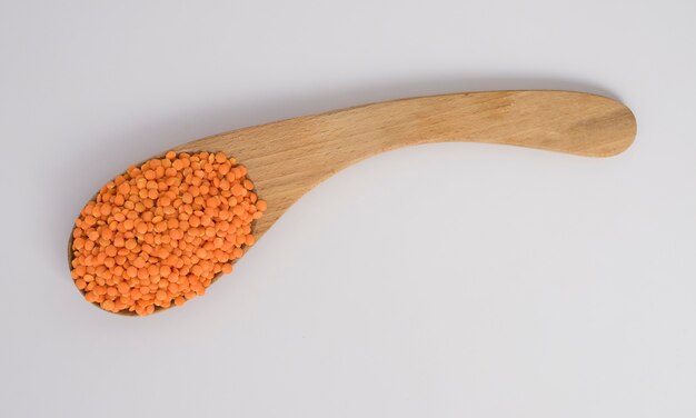 Red Lentils on a wooden spoon isolated on white background.